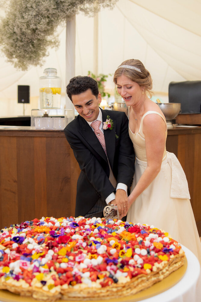 Bride and groom cutting their cake at their wedding at Hole Park Gardens, Bride wearing custom made wedding dress and belt by Kate Edmondson