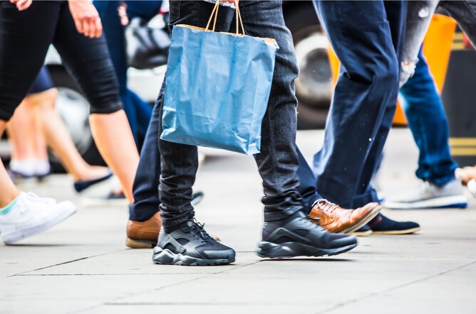 People walking in street carrying bags looking for shops - they will notice the shops that have had the best commercial signs Colchester can offer outside!