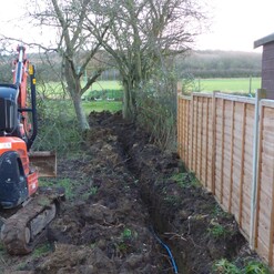 Image shows that we are laying a water pipe and mains power cable in a trench along the boundary line. At some point there is a plan for an outdoor shed and cooking area and power and water will be necessary.