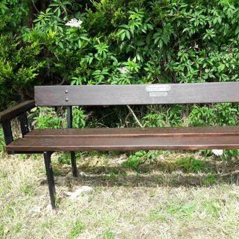 An old style 3 seater bench installed into grass verge area.