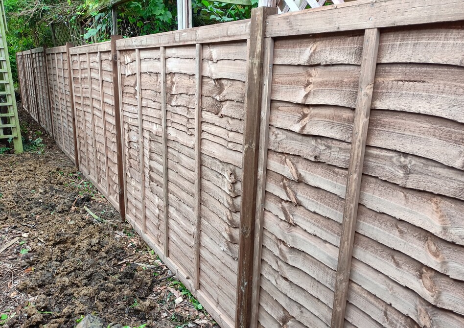 Image shows a run of overlap fence panels fitted to timber posts set into concrete foundations. This fence is aprt f a garden boundary between properties