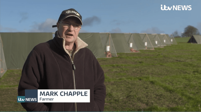 Mark Chapple standing in field at Redwoods Farm in front of chicken housing interviewed for ITN News