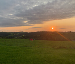 Image of a view from Redwoods Farm across the field with the sun setting over the hill in the distance