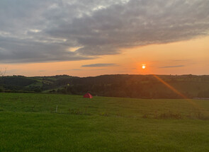 Image of a view from Redwoods Farm across the field with the sun setting over the hill in the distance